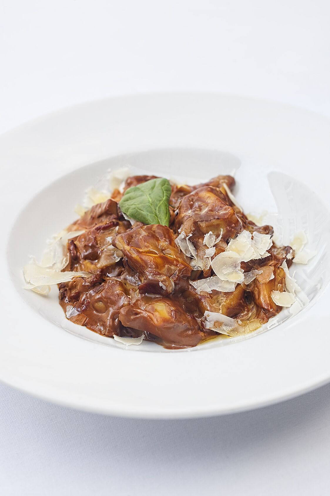 Un piatto bianco con un'insalata, forse di pollo, guarnita con una foglia di basilico e scaglie di formaggio.