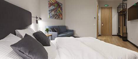 A modern hotel room with a large bed, a blue sofa, a small table with a plant, and a colorful abstract painting on the wall.