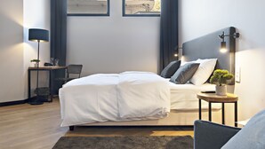 Un dormitorio moderno con una cama grande, una mesita de noche con lámpara, un escritorio pequeño y vistas al exterior a través de una ventana.
