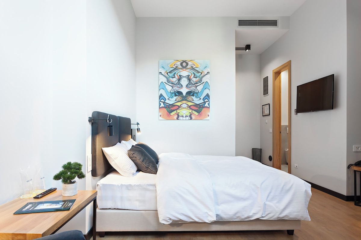 Une chambre d’hôtel moderne avec un lit, une table de chevet et un grand tableau abstrait accroché au mur.