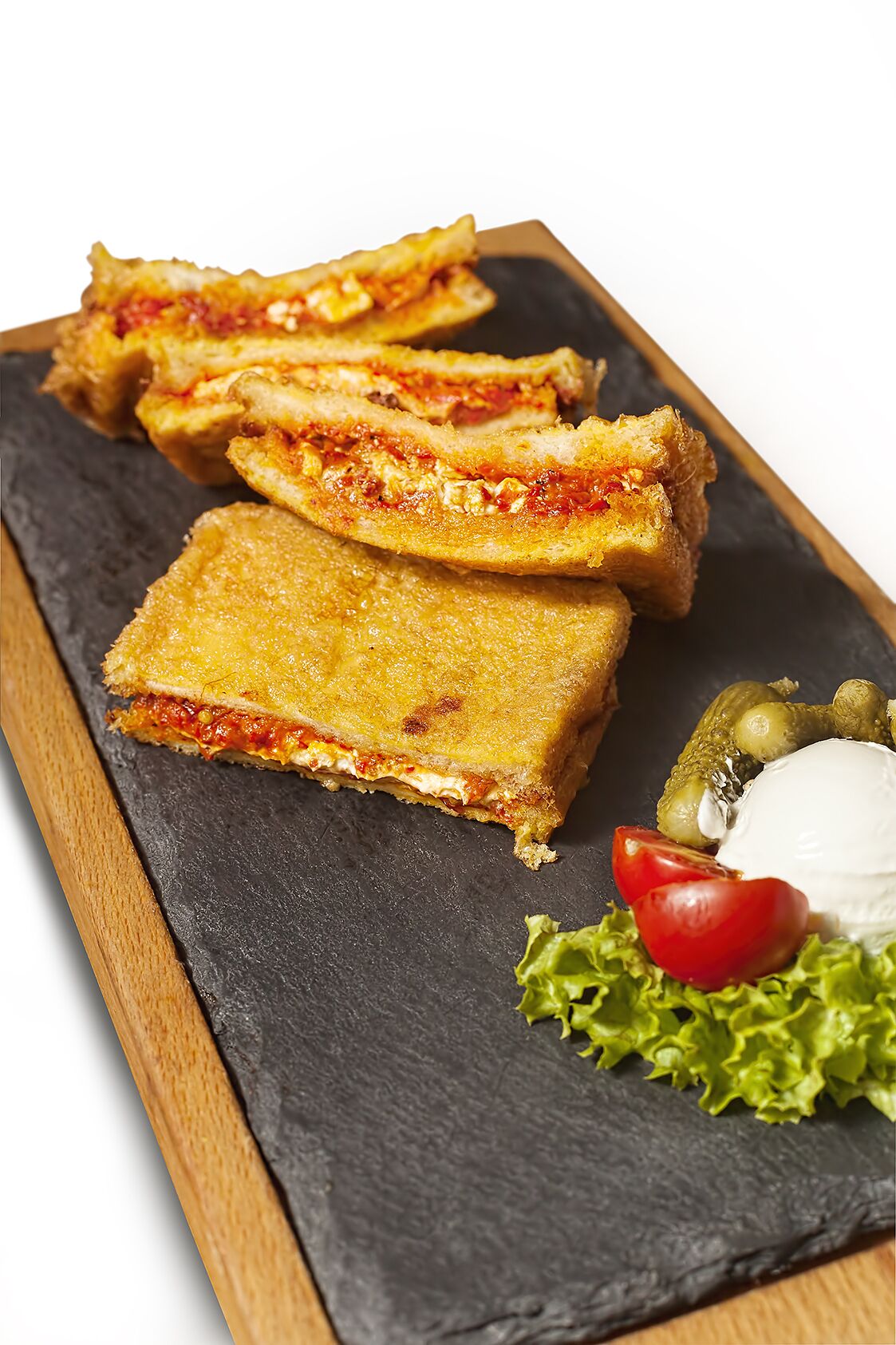 Un sándwich cortado por la mitad, sobre una tabla de servir de pizarra con borde de madera.