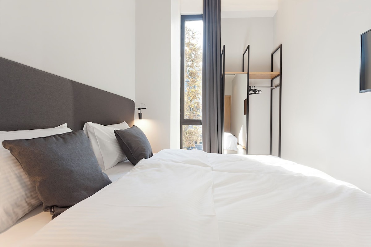 Une chambre d’hôtel moderne avec un grand lit, une tête de lit et une vue sur l’extérieur par une fenêtre.