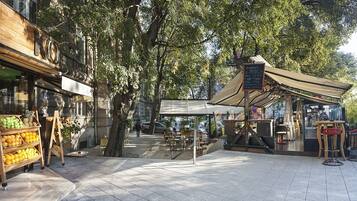 Un café al aire libre con mesa y sillas de madera, rodeado de árboles.