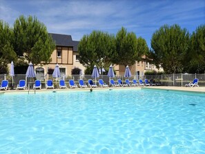 A swimming pool with blue chairs and umbrellas, surrounded by trees and buildings. - Holiday Home in Montignac near Lascaux II (Montignac)