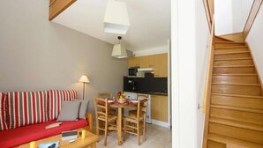 A compact living space with a sofa, dining table, chairs, a kitchen area, and a staircase. - Holiday Home in Montignac near Lascaux II (Montignac)