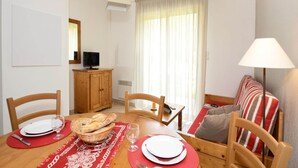A dining area with a wooden table set for two, a television on a wooden cabinet, and a window with curtains. - Holiday Home in Montignac near Lascaux II (Montignac)