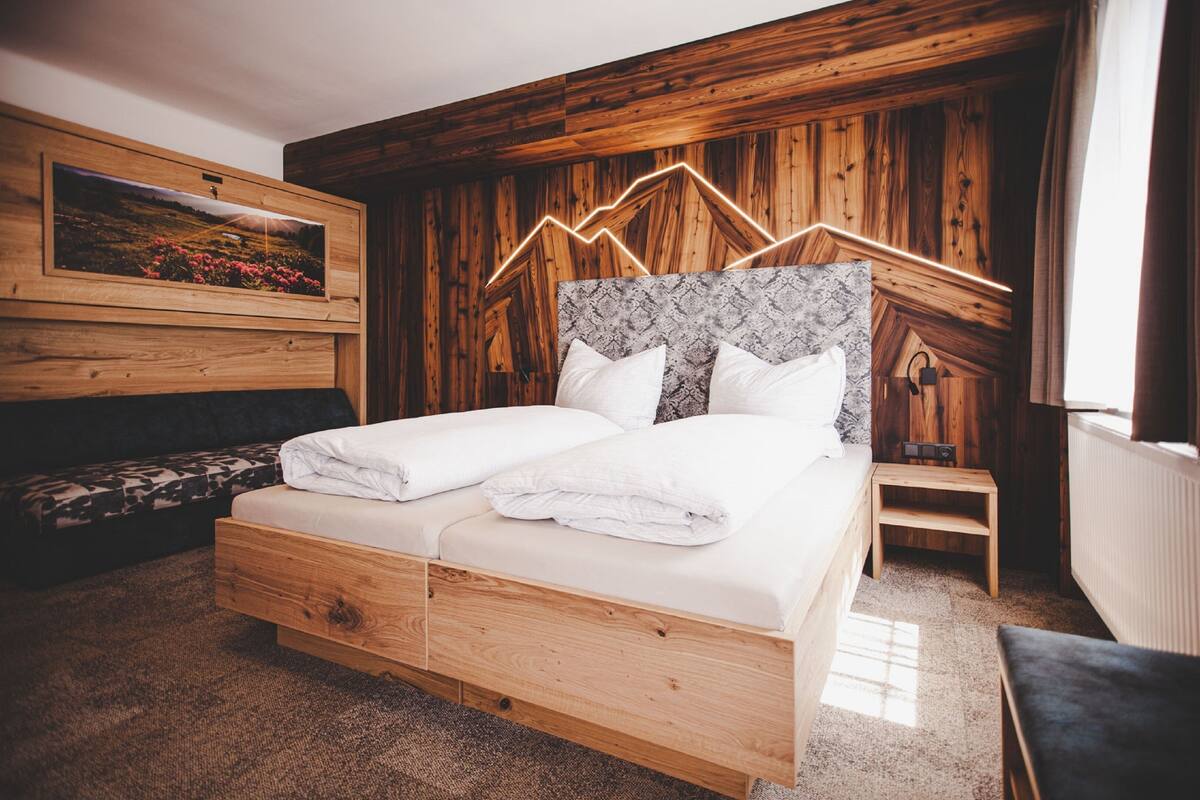A wooden-framed bed with white linens, a headboard with a geometric pattern, and a small bedside table.