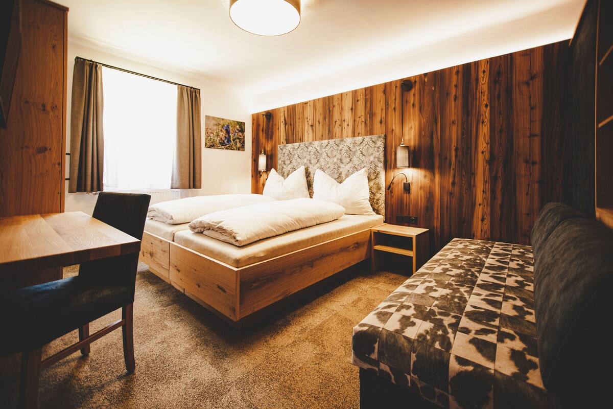 A wooden-paneled room with a bed, a desk, and a couch.