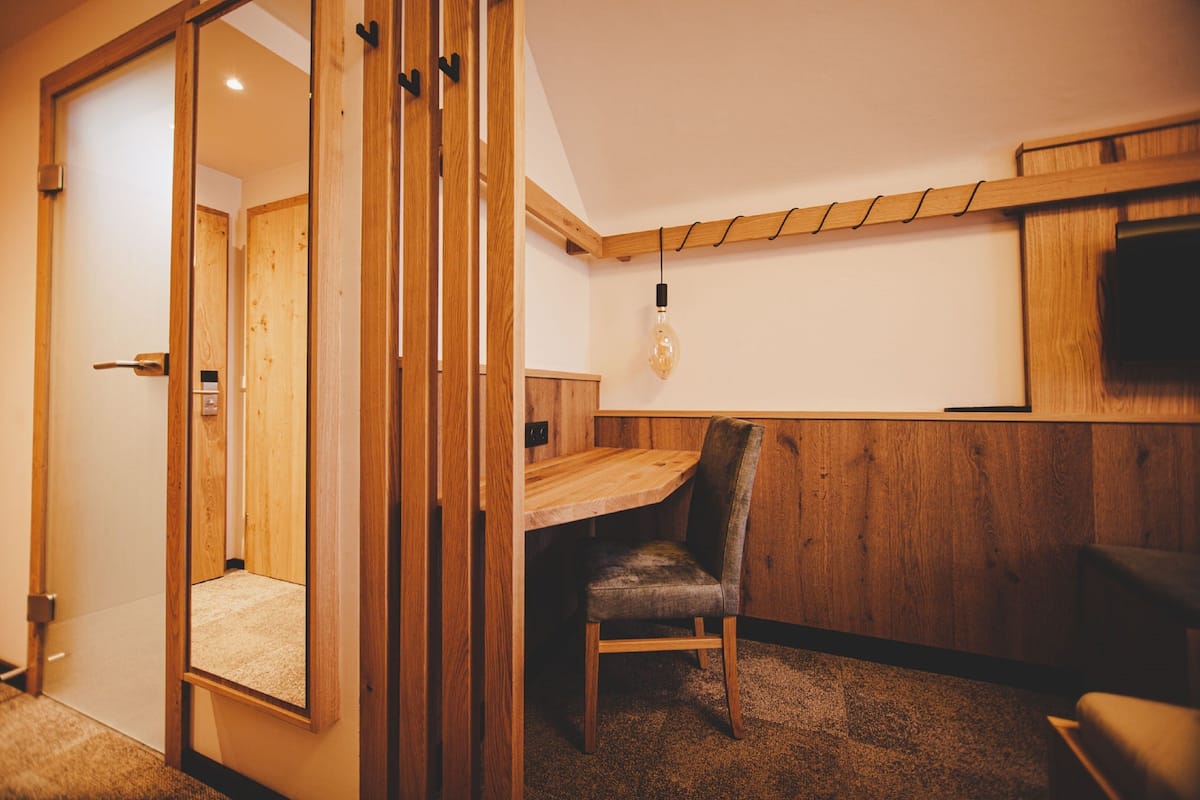 A wooden-framed room with a desk and chair, a hanging light bulb, and a mirror on the left wall.