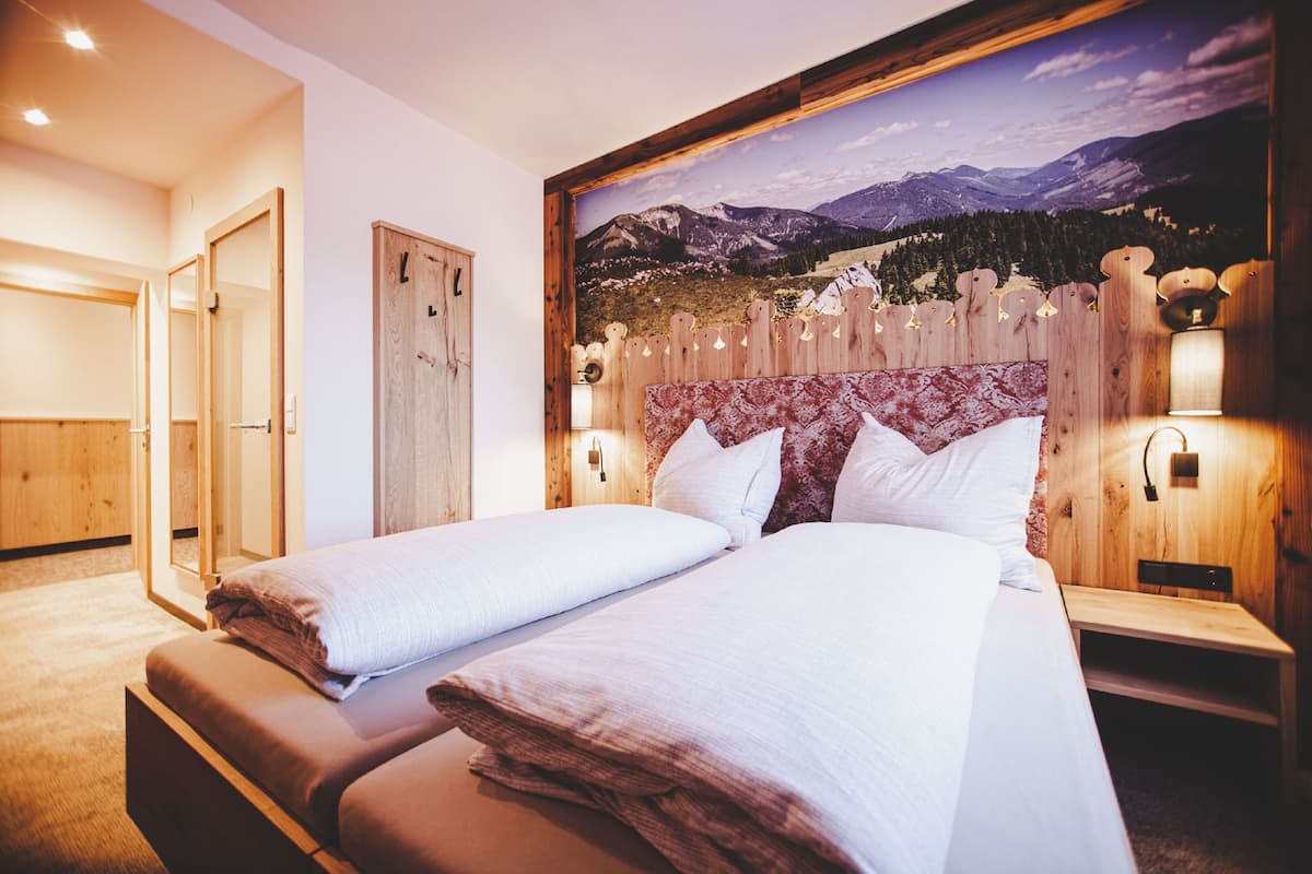 A bedroom with two beds, wooden headboard, wall-mounted lights, and a mountain landscape mural.