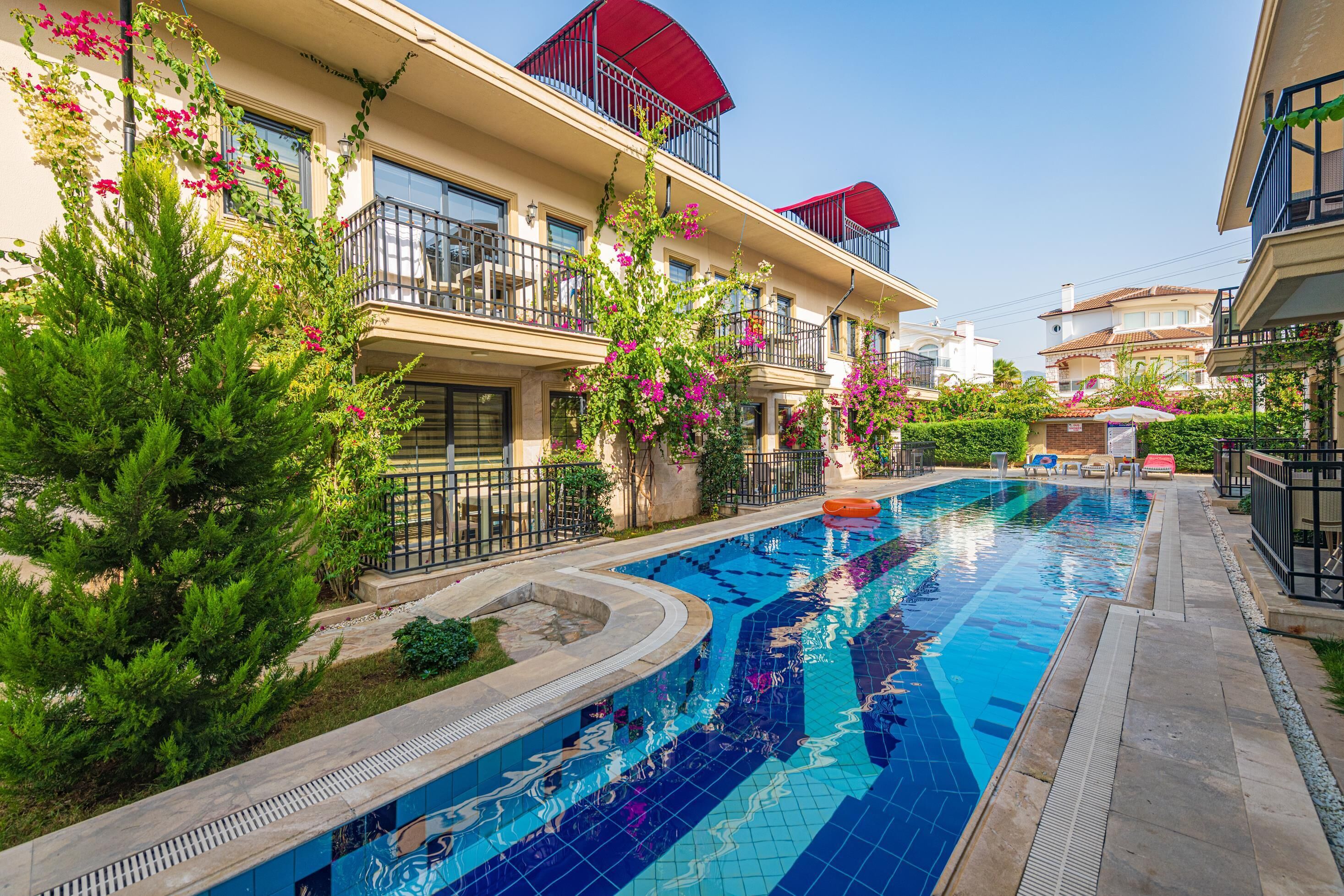 Une piscine entourée d’une végétation luxuriante et un bâtiment doté de balcons.