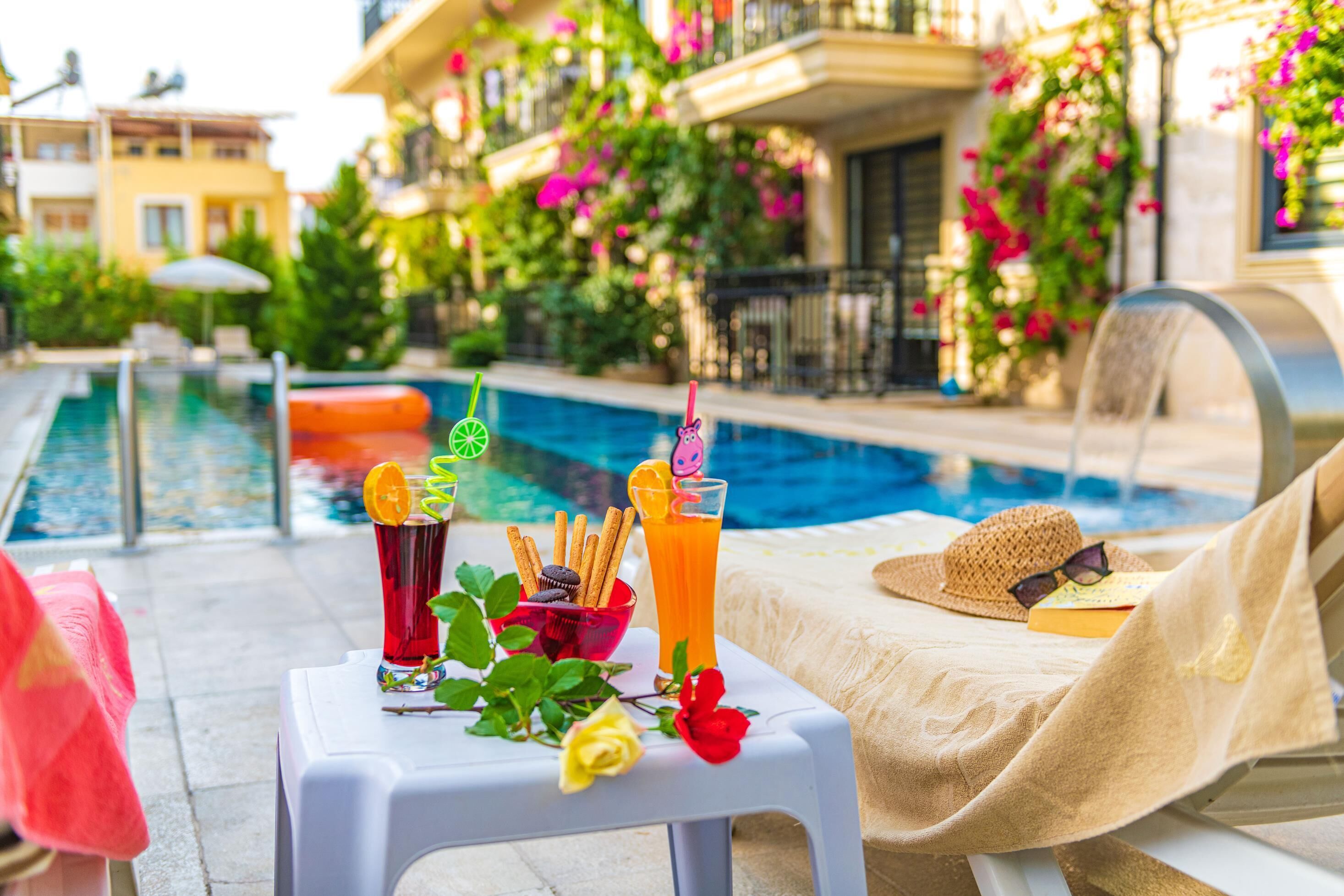 A poolside setting with a table holding drinks and snacks, a lounge chair, and a pool in the background.