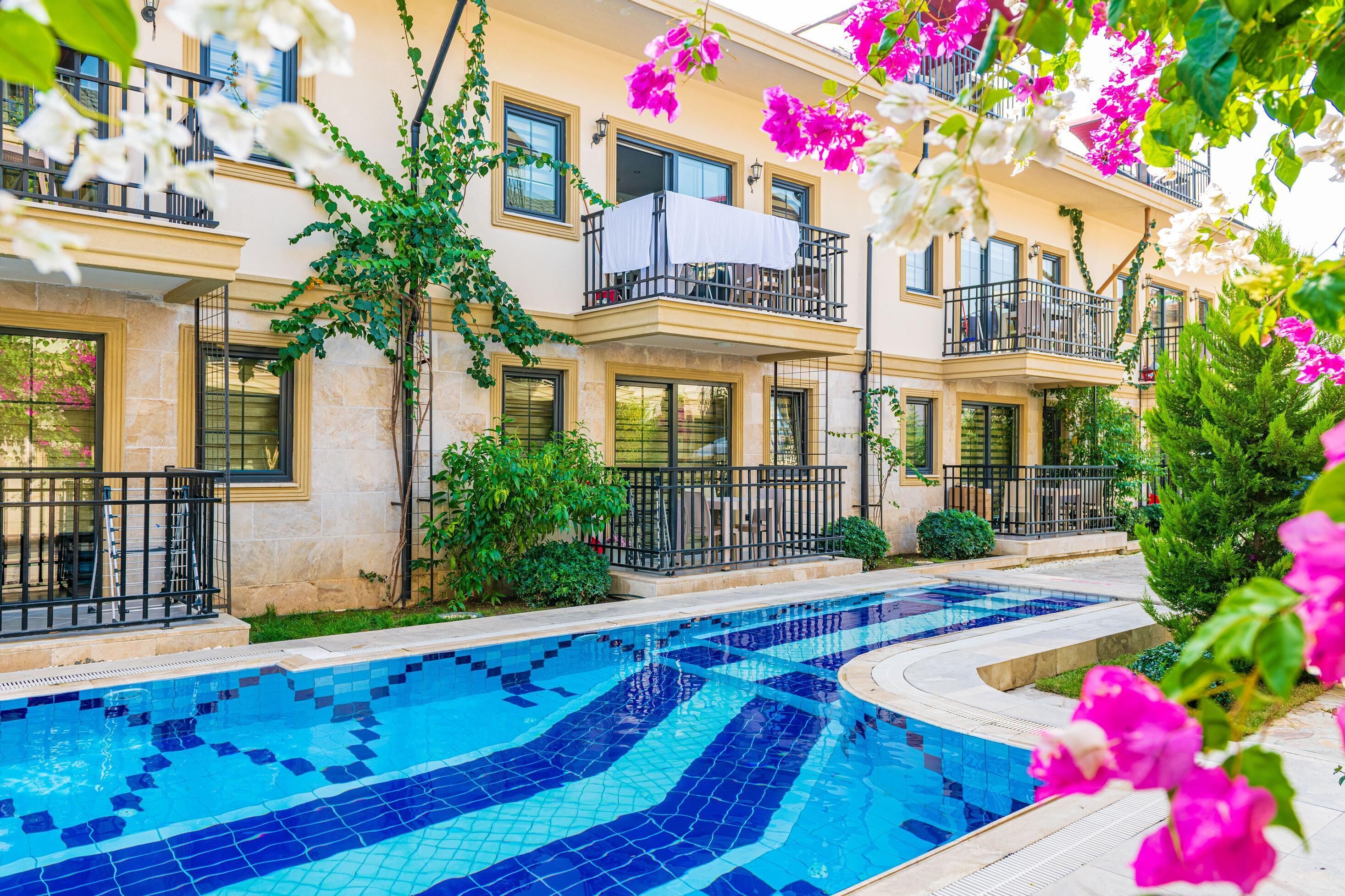 Edifício residencial com piscina, varandas e vegetação ao redor.