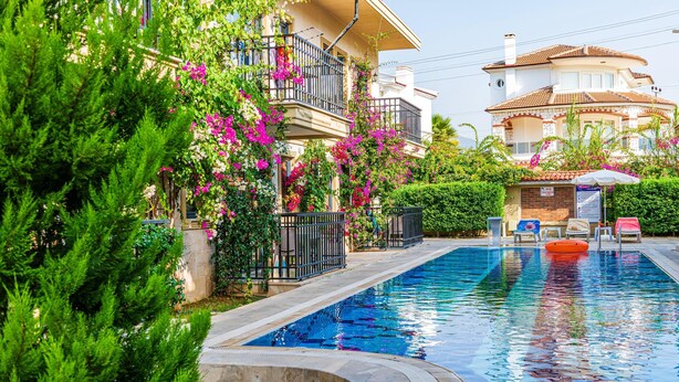 A swimming pool surrounded by lush greenery and a multi-story building with balconies.