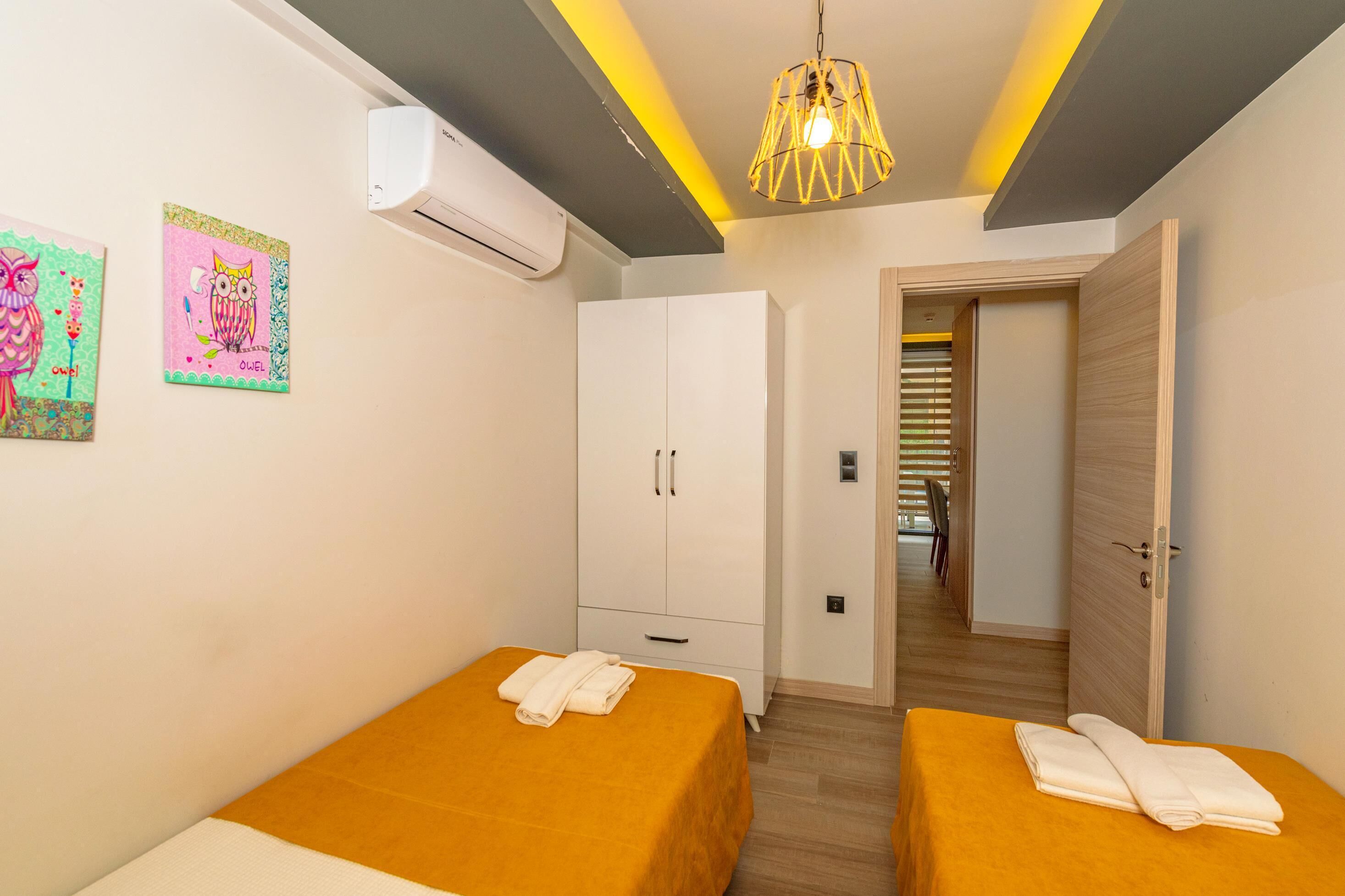 Una habitación con dos camas, aire acondicionado, un armario y un pasillo que lleva a otra habitación.