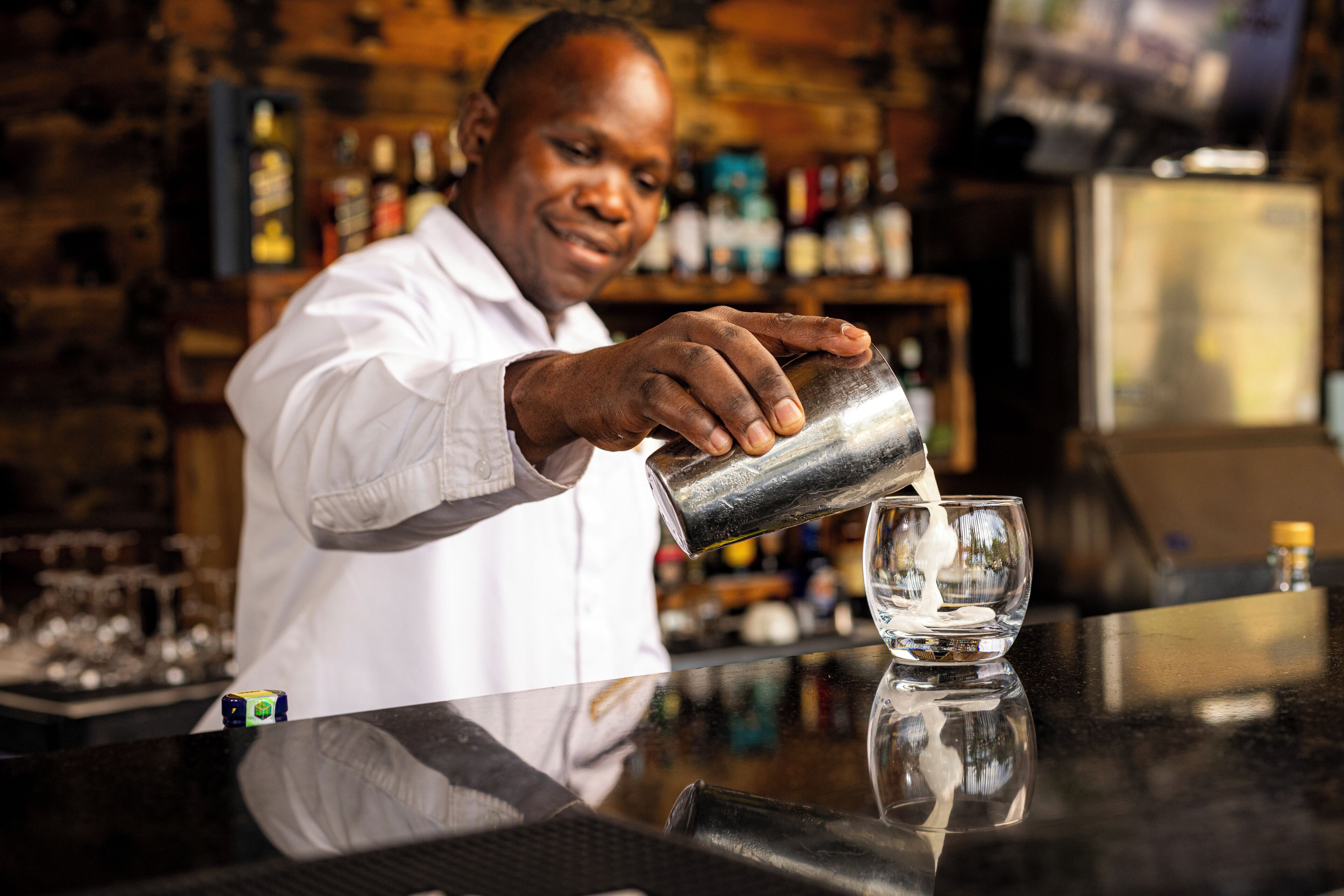 A person pouring a liquid into a glass at a bar counter.