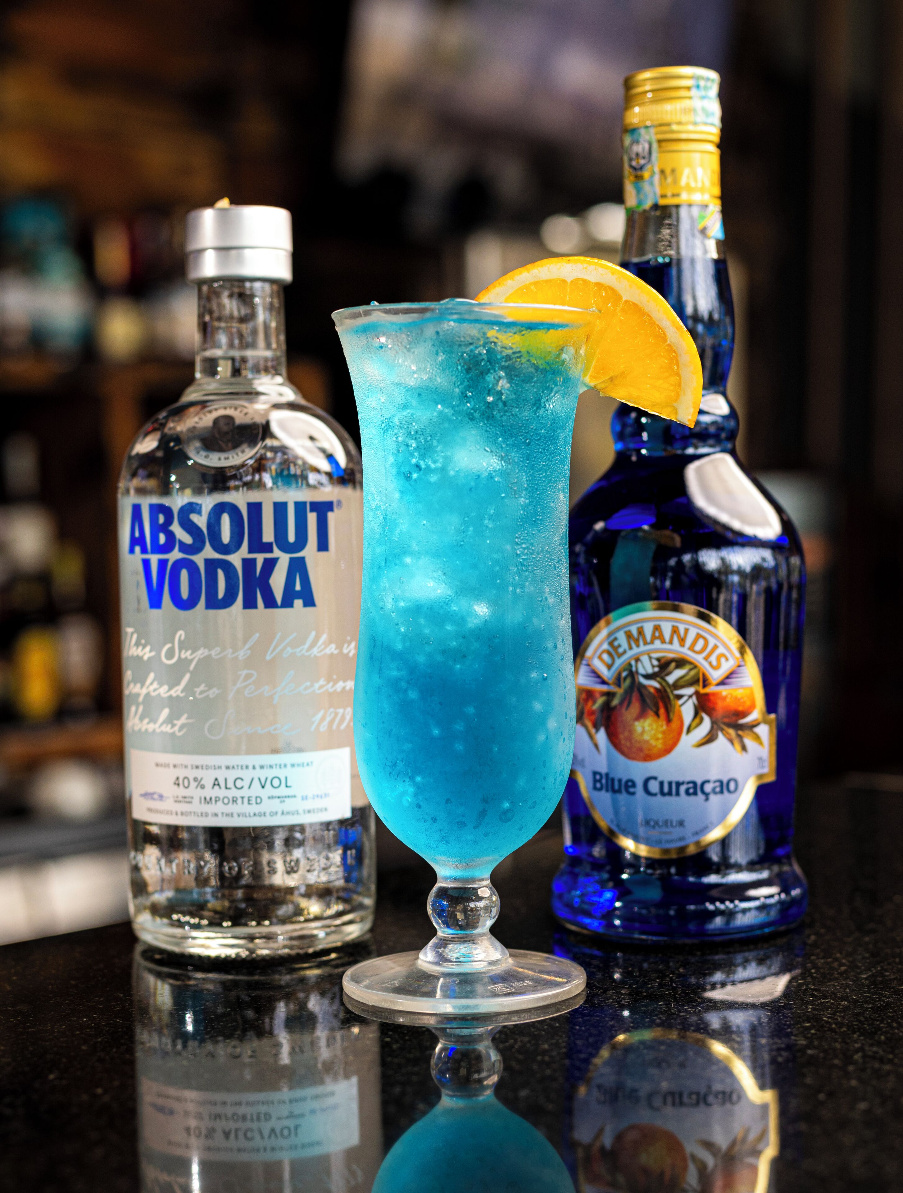 A bar setting with a blue cocktail, a bottle of Absolut Vodka, and a bottle of Blue Curaçao.