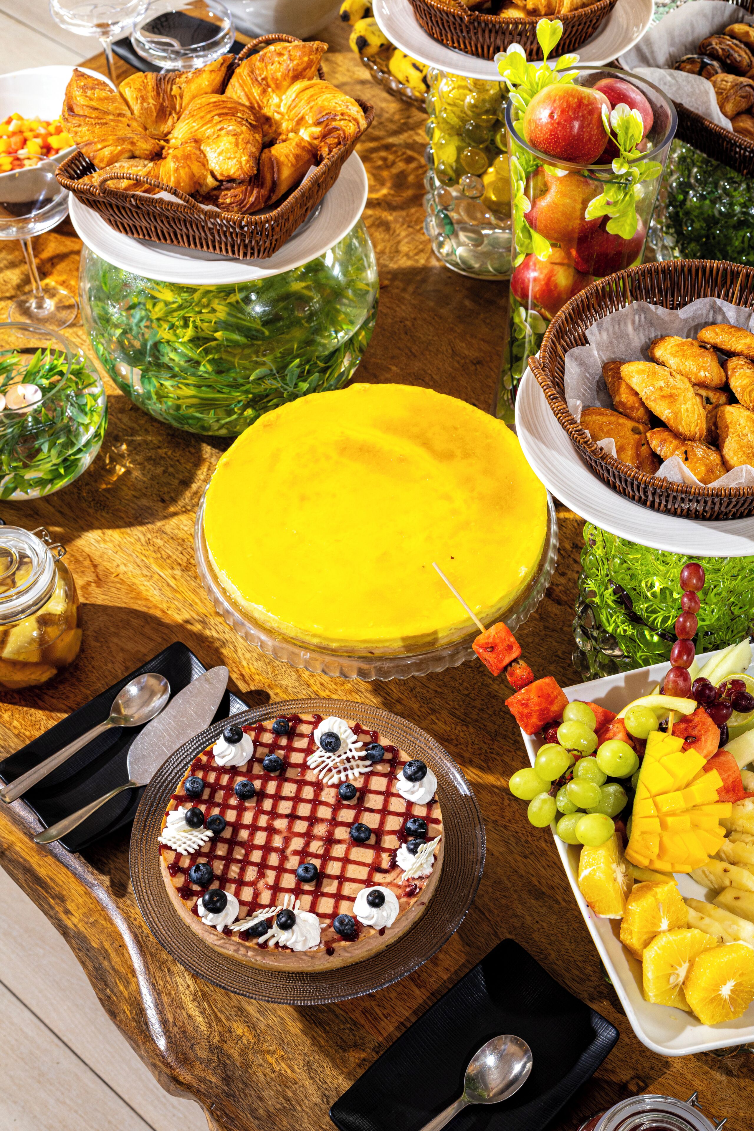 A variety of food items including pastries, a cheesecake, and fruit on a wooden table.