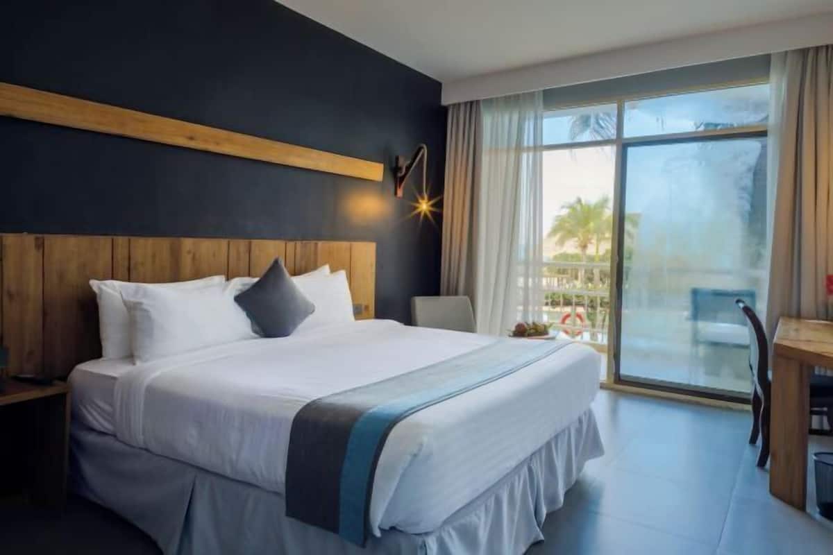 A hotel room with a large bed, a wooden headboard, a desk, and a view of the outdoors.