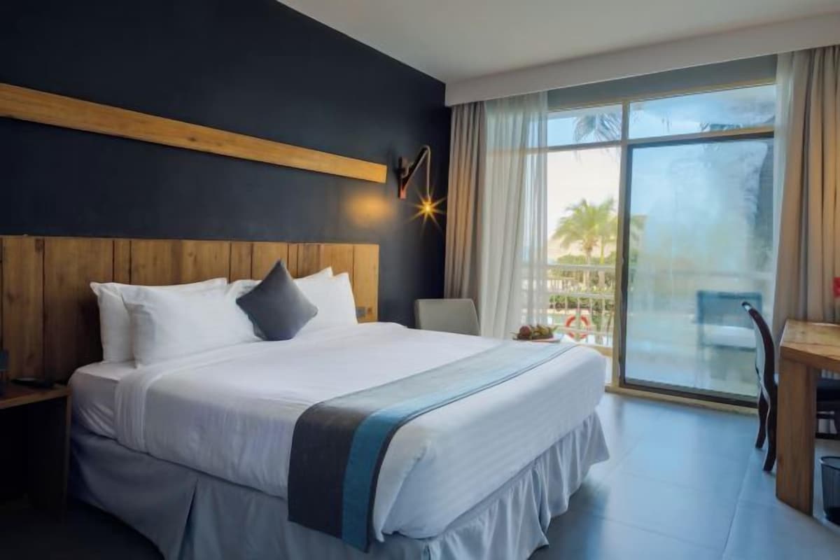 Habitación de hotel con una cama grande, cabecera de madera, escritorio y vistas al exterior.