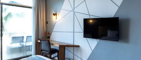 A hotel room with a bed, a desk, a TV, and a view of the outdoors.