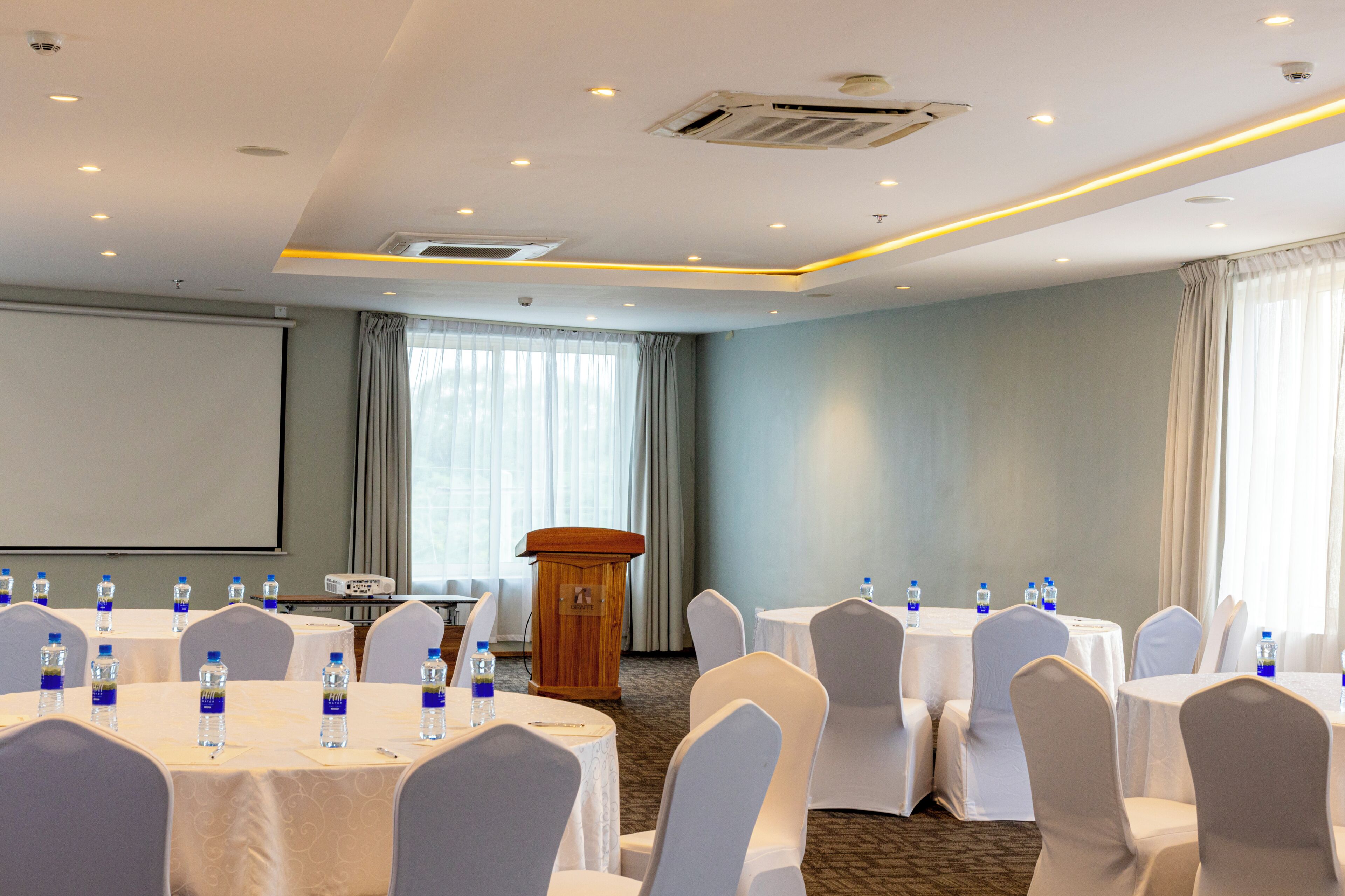 A conference room with round tables, chairs, a podium, and a projector screen.