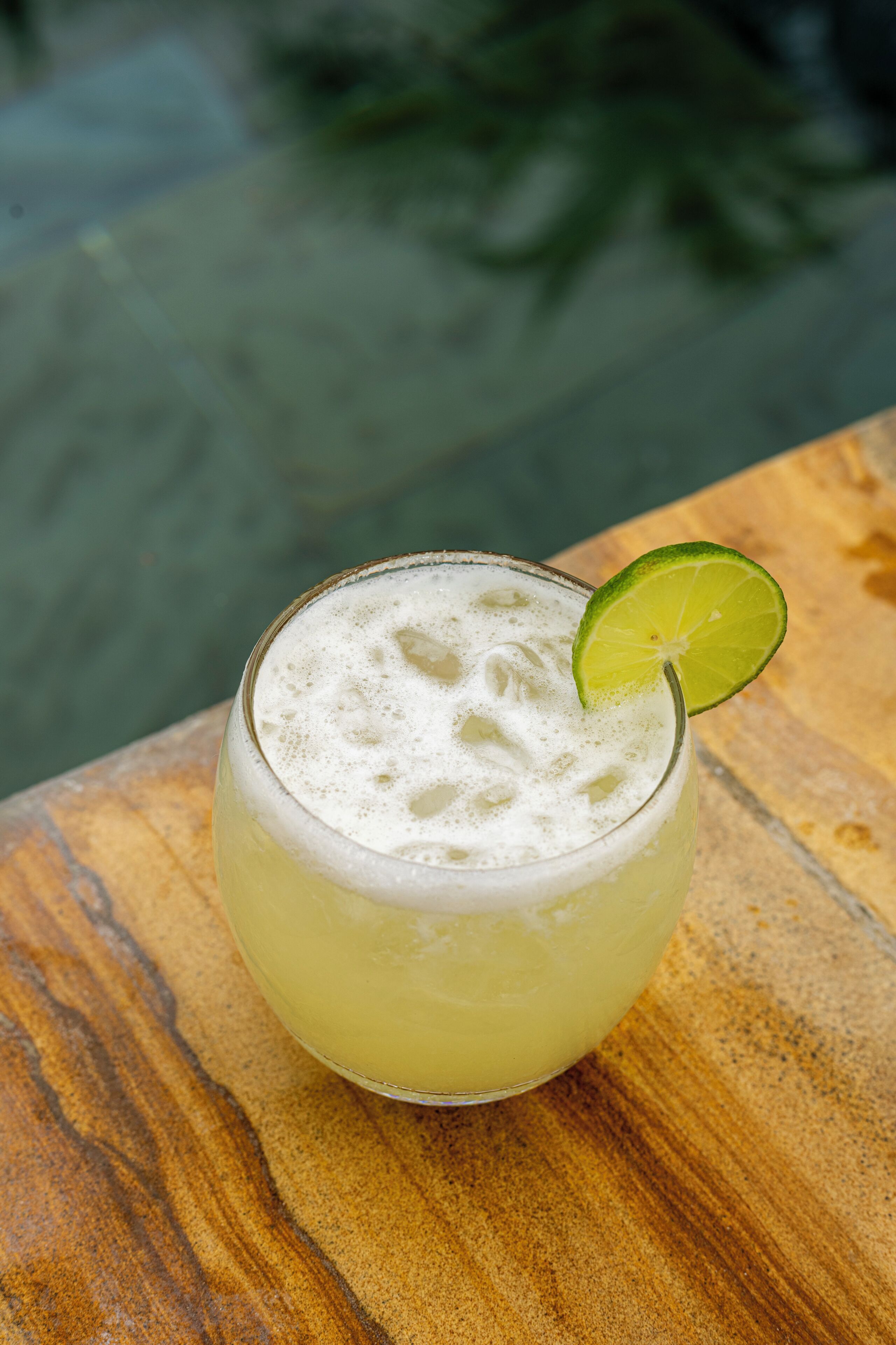 A glass of a light-colored beverage with a lime garnish on a wooden surface.