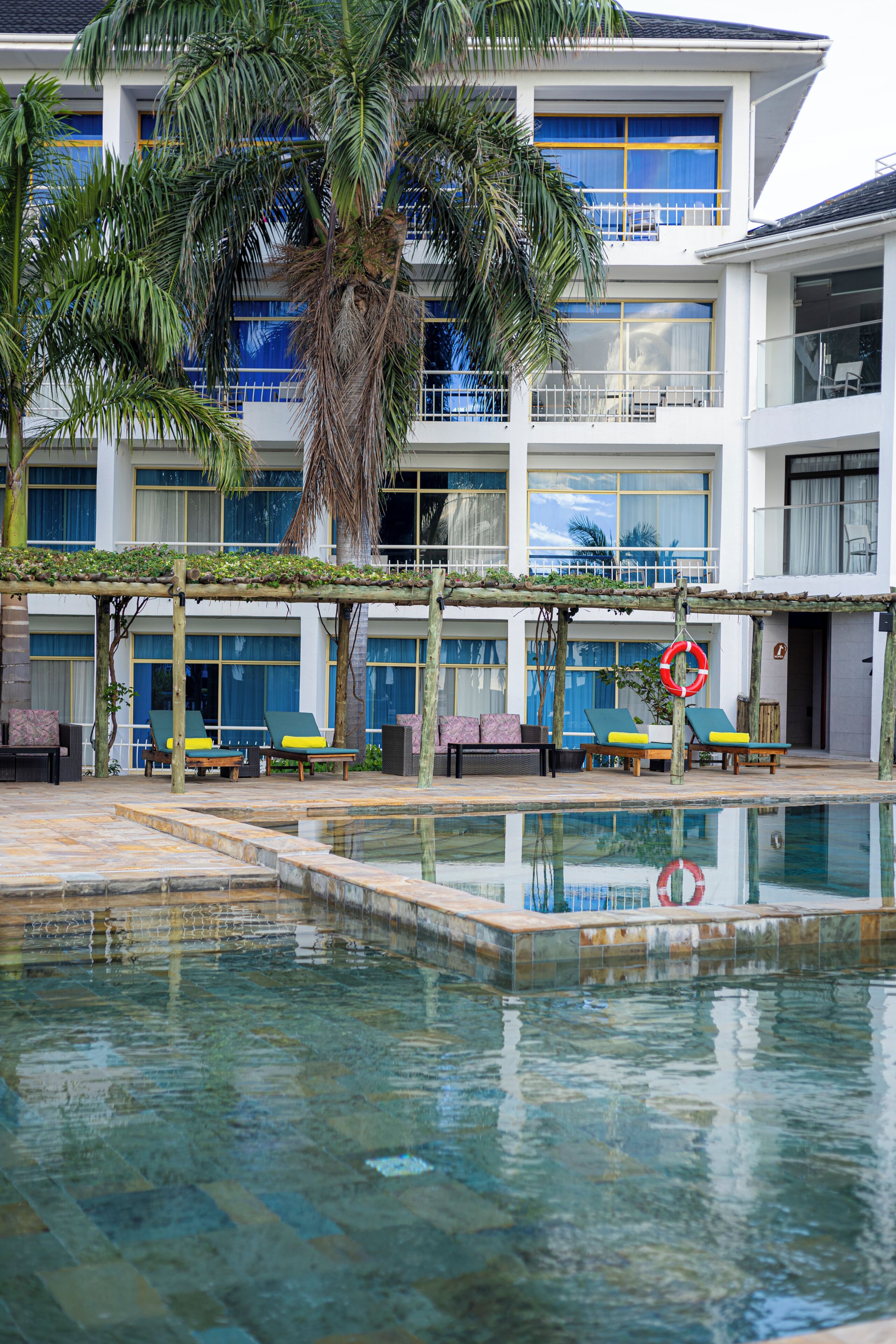 A pool area with lounge chairs, a palm tree, and a building with large windows and balconies.