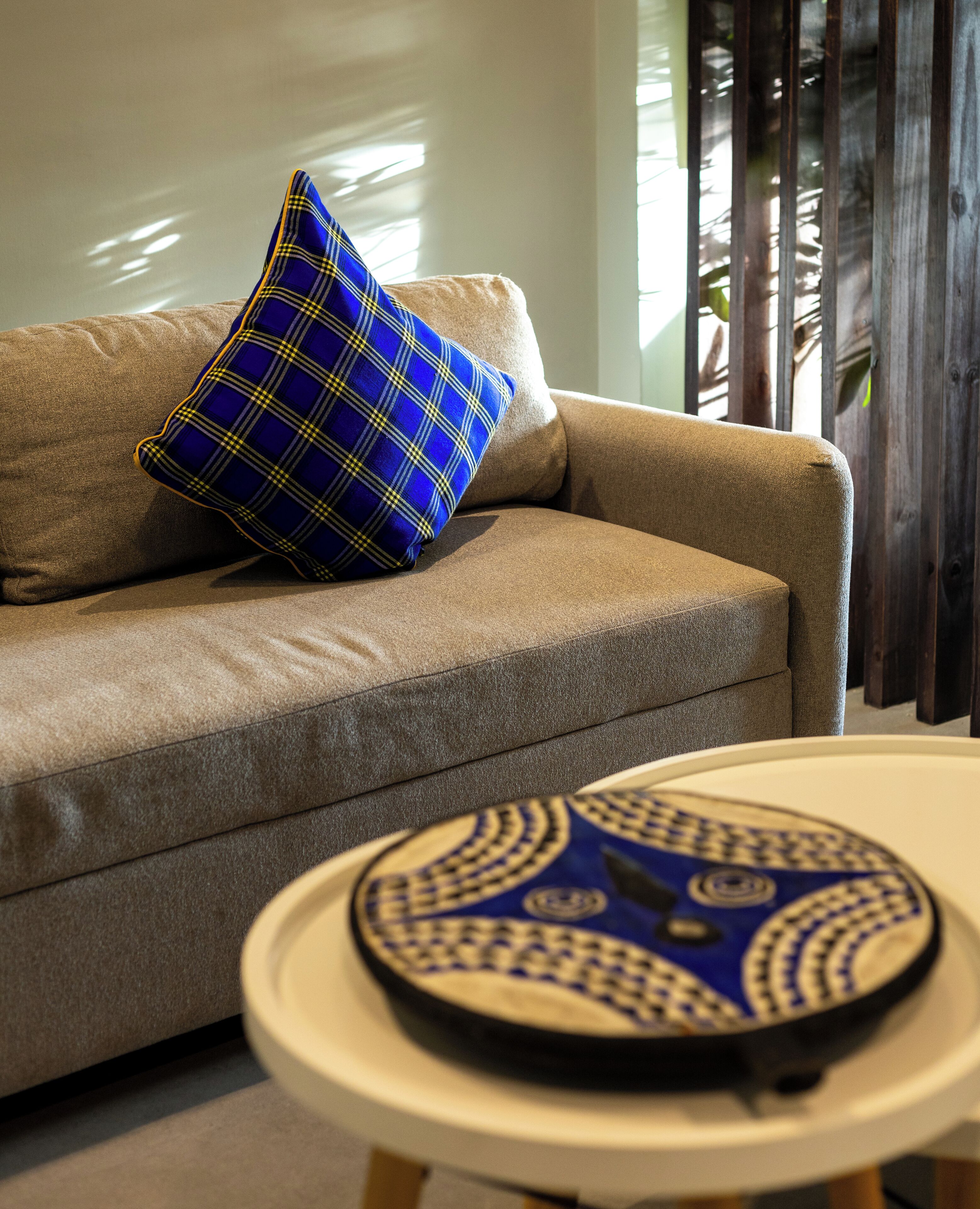 Un sofá color beige con un cojín azul de estampado escocés y una mesa redonda con una bandeja de diseño azul y blanco.