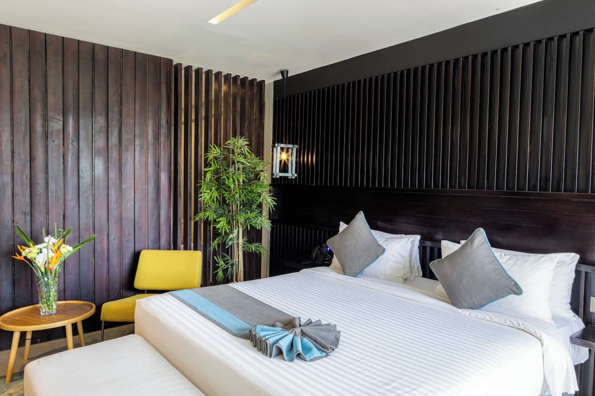 A hotel room with a bed, a small table, a chair, and a potted plant.