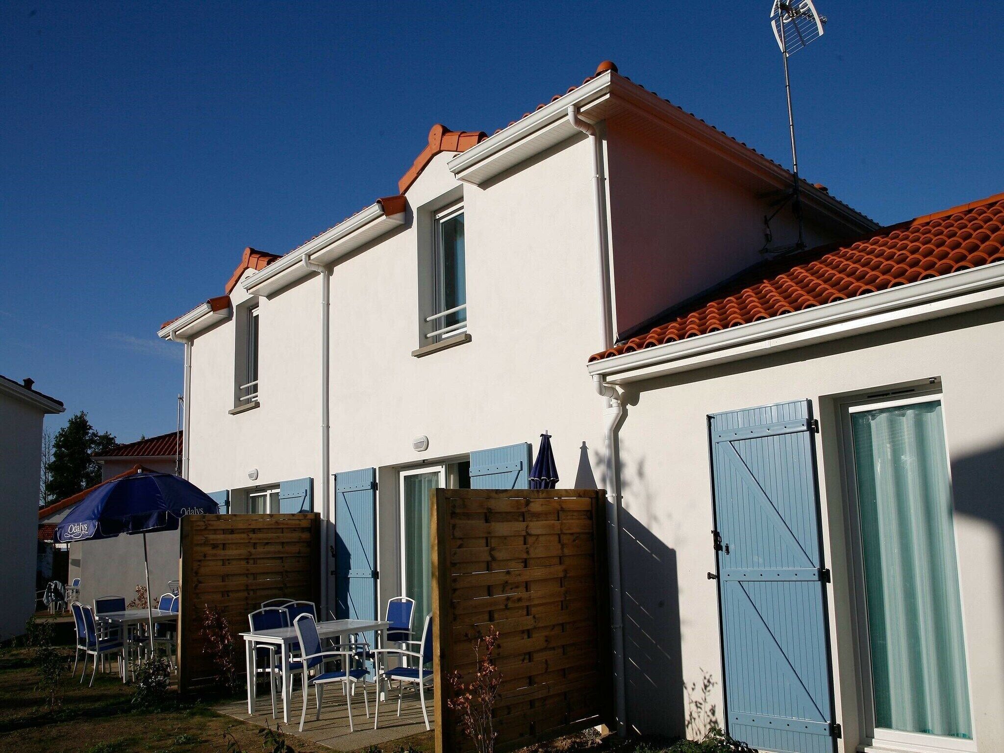 A two-story building with a red-tiled roof, a wooden fence, and a blue door.