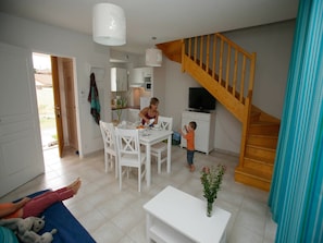 A spacious living area with a dining table, chairs, a TV, and a staircase.