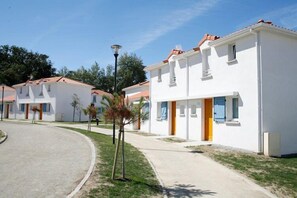 A row of white buildings with red-tiled roofs, a paved walkway, and a small tree.