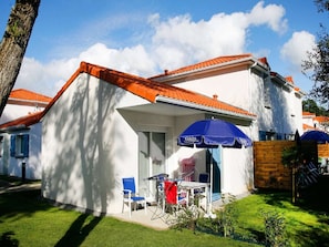 A residential building with a covered patio area, a blue umbrella, and outdoor furniture. - Apartment in France near the Beach (Saint Brevin L'océan)