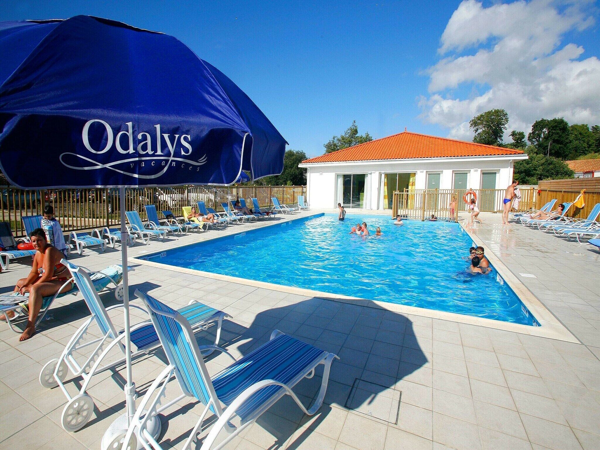 A swimming pool area with lounge chairs and a large umbrella.