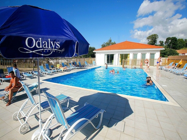 A swimming pool area with lounge chairs and a large umbrella.