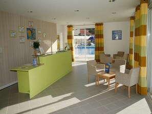 A reception area with a green desk, chairs, and a view of a pool. - Apartment in France near the Beach (Saint Brevin L'océan)