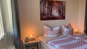 A bedroom with a bed, bedside tables, a nightstand, a wall-mounted painting, and a window with curtains. - Vacation apartment Bad Wilsnack (Bad Wilsnack)