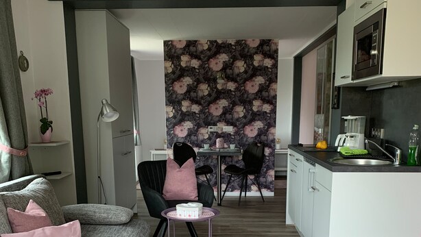 A modern living room with a grey sofa, a pink rug, and a dining area with a table and chairs. - Vacation apartment Bad Wilsnack (Bad Wilsnack)