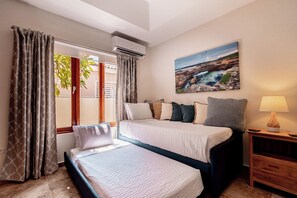 A hotel room with two beds, a painting, a lamp, and an air conditioning unit. - Pool Oasis: 3BR Home w/ Patio near Arashi Beach (Noord)
