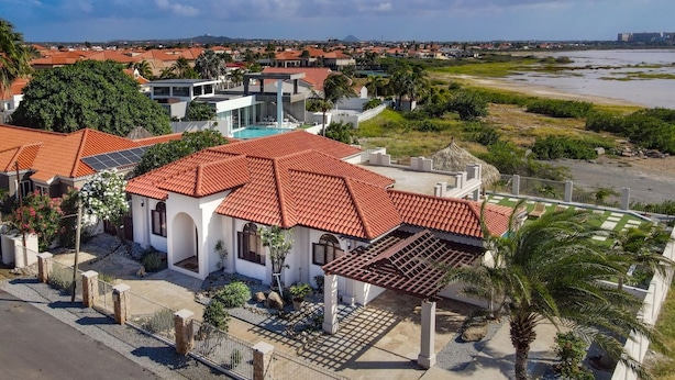 Quartiere residenziale con case dotate di tetti in tegole rosse, una piscina e una spiaggia sullo sfondo.