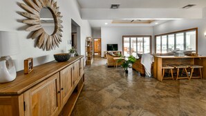 Un'ampia zona giorno con un mobile in legno, uno specchio decorativo e un angolo salotto con tavolo e sedie.