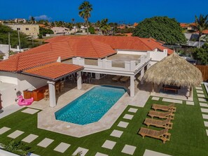 A residential property with a swimming pool, outdoor seating, and a thatched-roof structure. - Pool Oasis: 3BR Home w/ Patio near Arashi Beach (Noord)