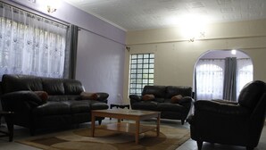 A living room with two black leather sofas, a wooden coffee table, and a black armchair. - Sweet Apple Mansion Naivasha (Naivasha)