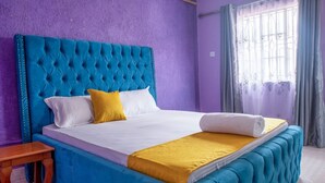 A bed with a tufted headboard, a wooden nightstand, and a window with curtains. - Sweet Apple Mansion Naivasha (Naivasha)