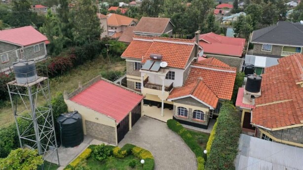 A residential area with houses featuring red-tiled roofs, surrounded by greenery and a distant body of water. - Sweet Apple Mansion Naivasha (Naivasha)