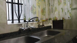 A kitchen with a double sink, a faucet, and a window with floral curtains. - Sweet Apple Mansion Naivasha (Naivasha)