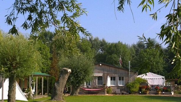 A wooden house with a porch, a covered picnic area, and a white tent.