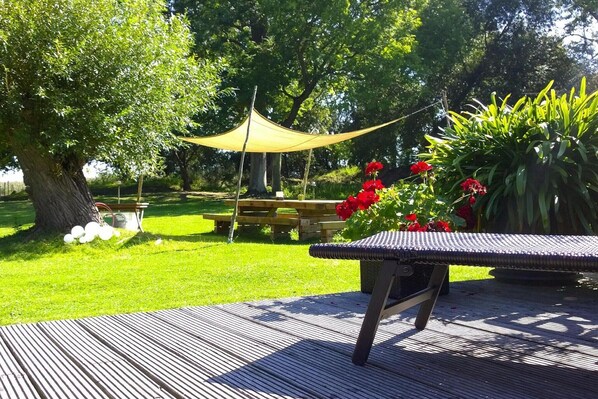 A garden patio with a table and chairs, surrounded by greenery and a tree.