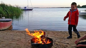 A beach scene with a campfire, boats, and a person in a red jacket.